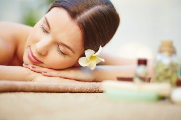 Relaxed female with frangipani flower in hair lying in spa salon